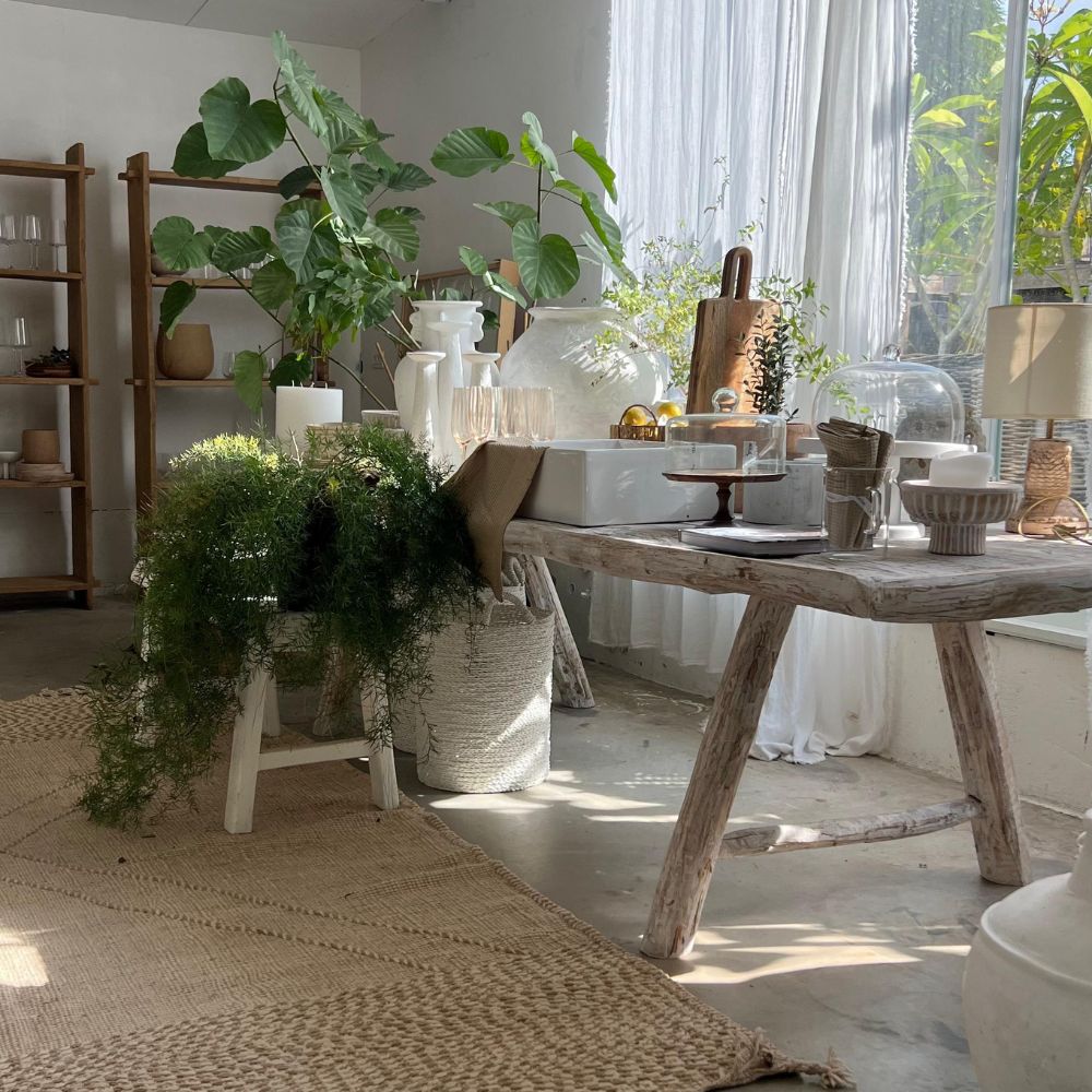 חדר מואר בשמש עם ריהוט עץ כפרי, הכולל את Fine Lab Home שולחן אוכל מעץ בגימור Whitewash - שני גדלים, צמחים מקורה, כלי חרס ושטיחים ארוגים ליצירת אווירה טבעית ונעימה.