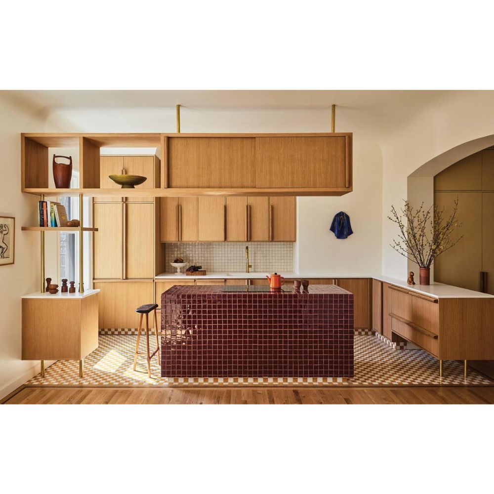 מטבח עכשווי עם ארונות עץ, אי עם אריחים אדומים, מדפים פתוחים, אלמנטים דקורטיביים ואגרטל – המבטא את תמצית "ספר עיצוב New York Interiors" של Fine Lab Home להשראה העיצובית הבאה שלכם.