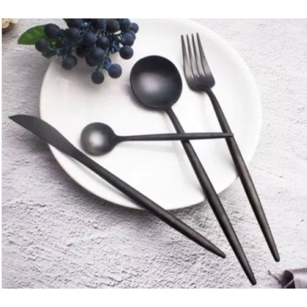 צלחת לבנה עם סט סכו"ם 24 חלקים - שחור מט של Fine Lab Home, העשוי מנירוסטה איכותית — כף, מזלג, סכין ומצקת — מסודרים בקפידה, וענבים בצד ליצירת עיצוב מינימליסטי.