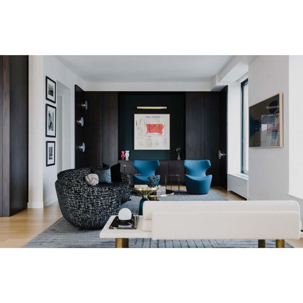 סלון מודרני עם קיר כהה, אמנות מופשטת, כיסאות כחולים ושחורים, ספה לבנה וחלונות גדולים — השראה מושלמת מתוך ספר העיצוב New York Interiors של Fine Lab Home.