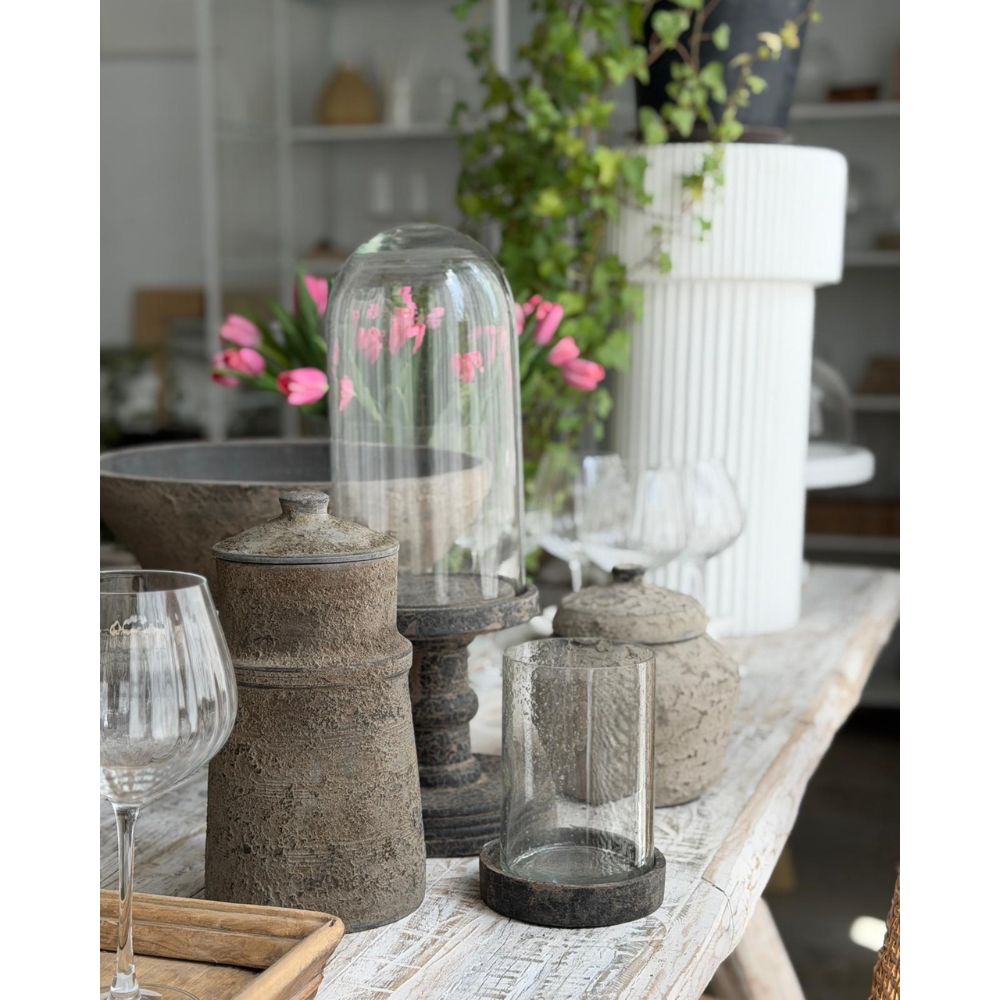 שולחן כפרי עם כלי אבן, כוסות יין וצבעונים ורודים, שבמרכזו ניצב "פעמון זכוכית צר על רגל מעץ" מבית Fine Lab Home, המהווה פריט דקורטיבי מקסים.