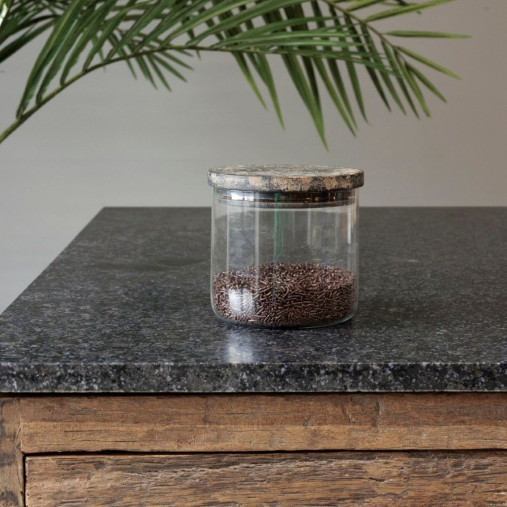 צנצנת זכוכית עם מכסה עץ – בשלושה גדלים מבית Fine Lab Home, עם זרעים חומים, מונחת על משטח אבן כהה לצד מגירת עץ, וצמח ירוק ברקע.