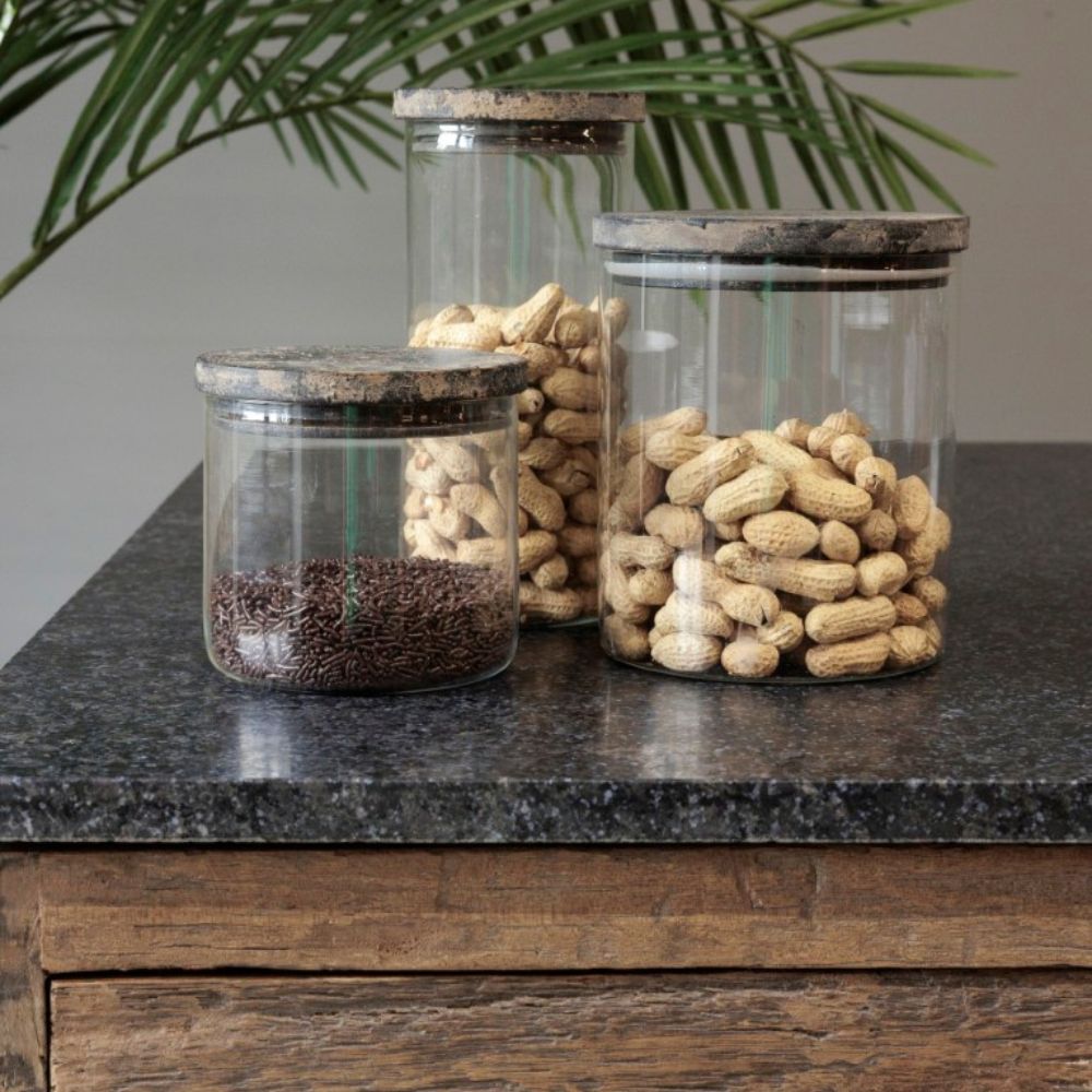 שלוש צנצנות זכוכית עם מכסה עץ מבית Fine Lab Home עומדות על משטח כהה; בשתיים מהן יש בוטנים לא קלופים, ובאחת יש סוכריות שוקולד.