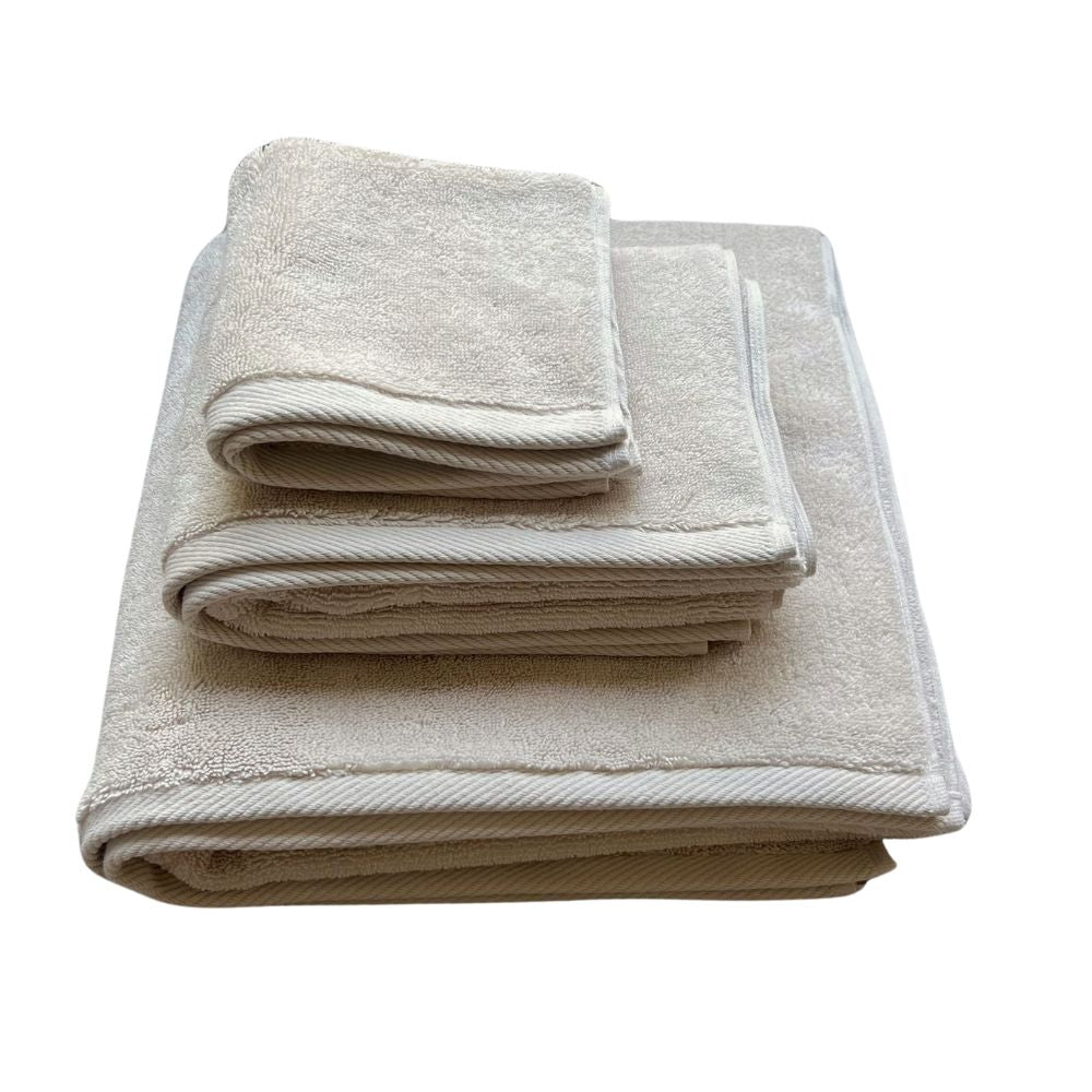 ערימה של שלוש מגבות כותנה מקופלות בקפידה, כולל מגבת גוף איכותית ומפנקת בצבע חול מבית Fine Lab Home, מוצגות על רקע לבן.