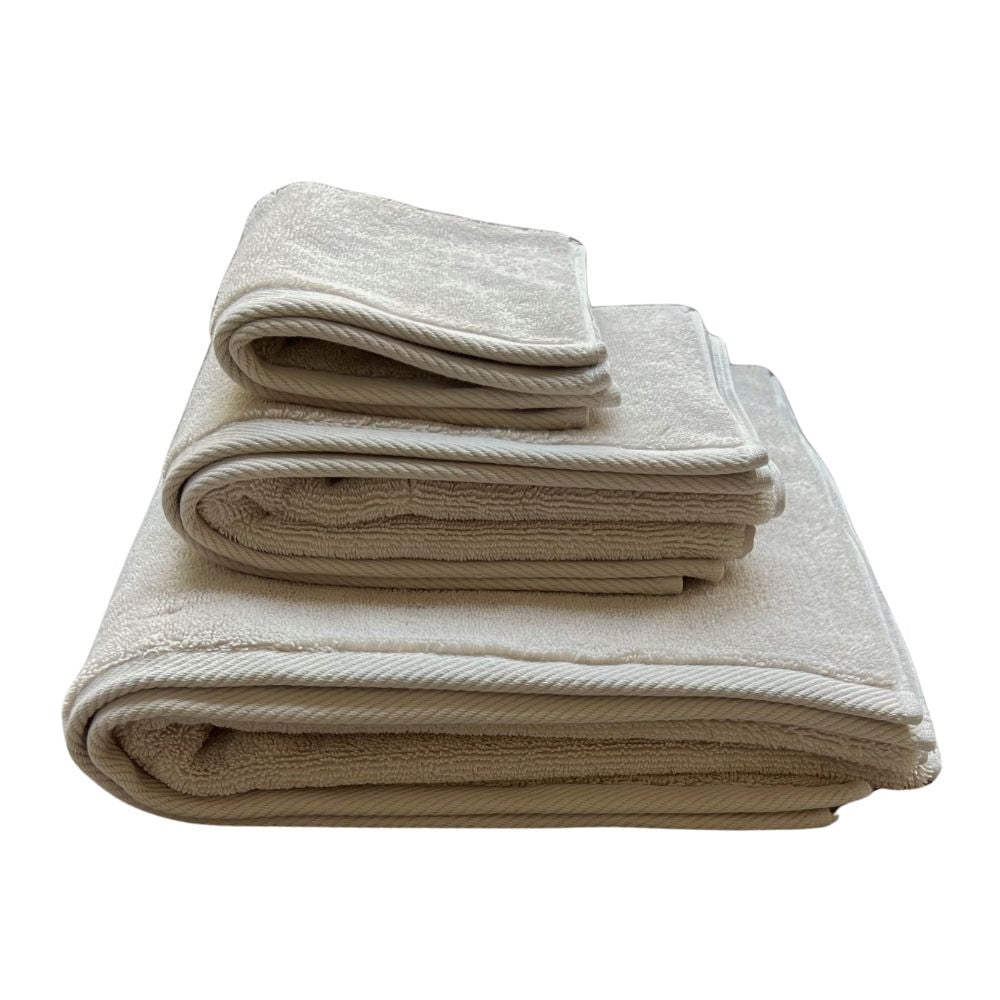 שלוש מגבות גוף איכותיות - צבע חול מבית Fine Lab Home מונחות זו על גבי זו על רקע לבן.