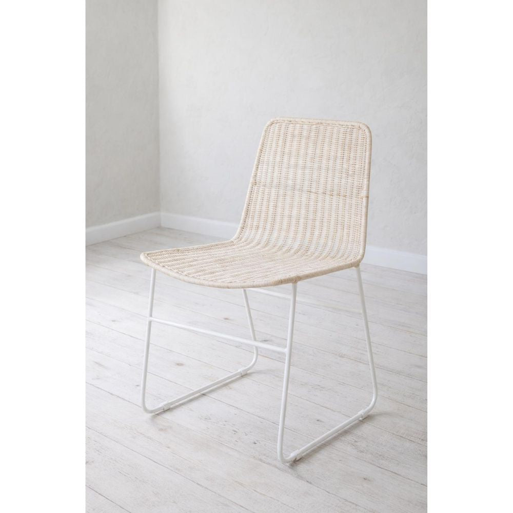 כיסא האוכל "ראטן רגלי מתכת" מבית Fine Lab Home מתאפיין בעיצוב מינימליסטי, עם מושב ומשענת קלועים מרטאן על רגלי מתכת לבנות ודקות, המוצג על רצפת עץ בהירה בחדר מואר וריק.