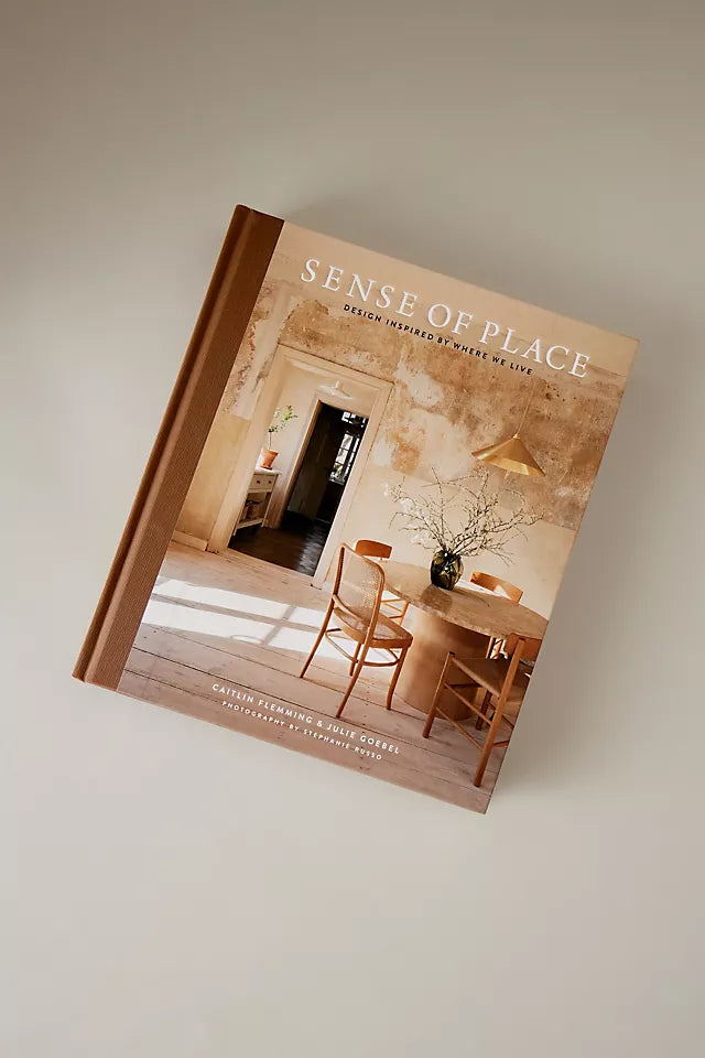 עטיפת הספר "ספר עיצוב sense of place" מאת Fine Lab Home, המציגה פינת אוכל כפרית עם ריהוט מעץ, קירות בהירים, אגרטל עם ענפים ואור טבעי רך. כולל את שם הספר ושמות המחברים.