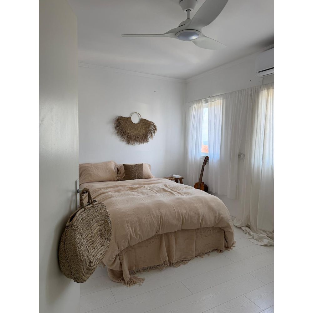 חדר שינה מינימליסטי עם סט מצעים טטרה זוגי בצבע חול – סדין 1.80 מבית Fine Lab Home בגוון בז', קישוט קיר עגול ארוג, גיטרה ליד החלון, וילונות לבנים ותיק קש התלוי על הדלת.