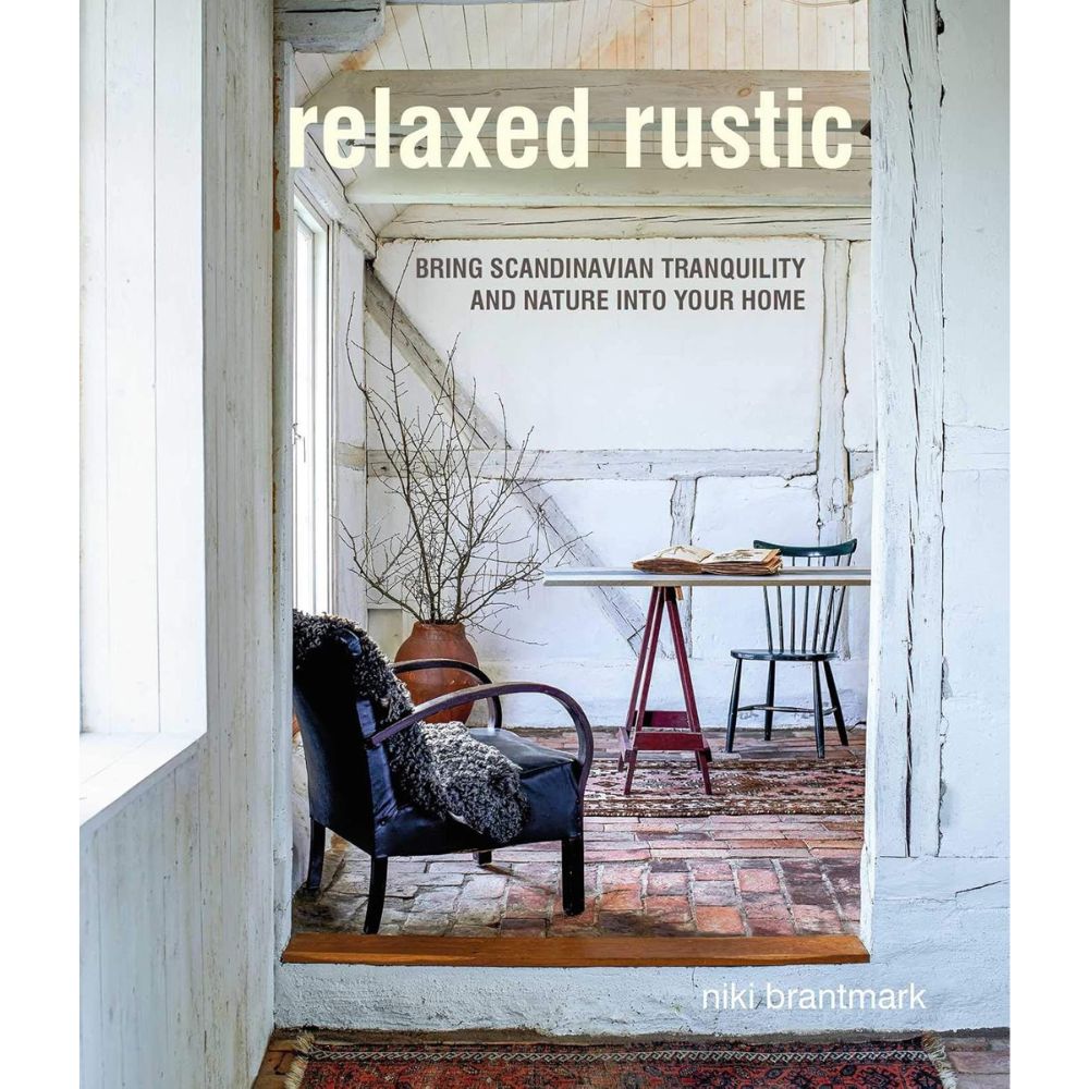 כריכת הספר "Relaxed Rustic" מאת Fine Lab Home, המציגה עיצוב פנים נעים בסגנון סקנדינבי עם כיסא, שולחן עץ, אגרטל עם ענפים ושטיחים בשכבות.