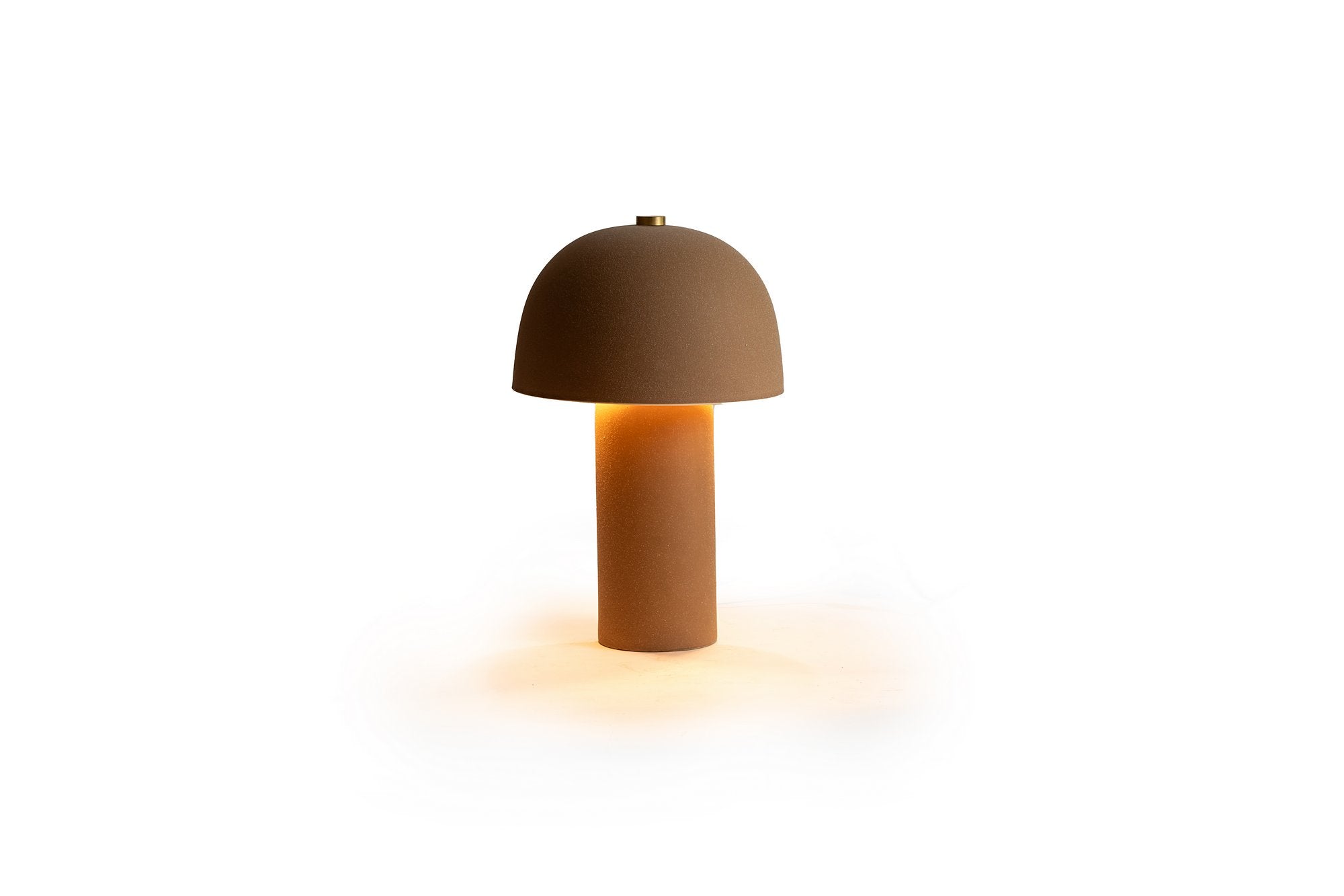 מנורת שולחן חול חומה מבית Fine Lab Home פולטת אור חם, ממוקמת על רקע לבן חלק.