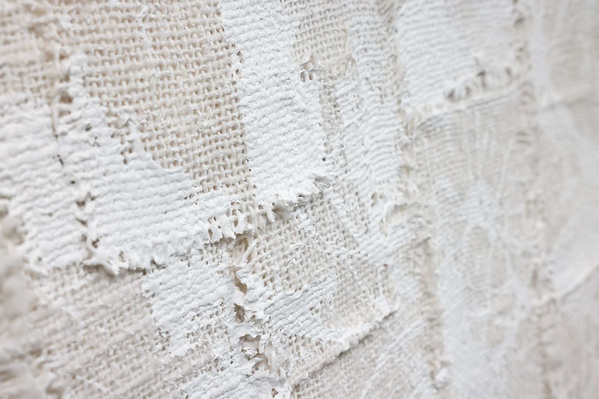 אומנות קיר - Woven White של Fine Lab Home כולל מסגרת מלבנית עם טלאים לבנים מרקמים וחופפים על רקע ניטרלי ומסגרת עץ, המוצגת באלגנטיות על רקע לבן.