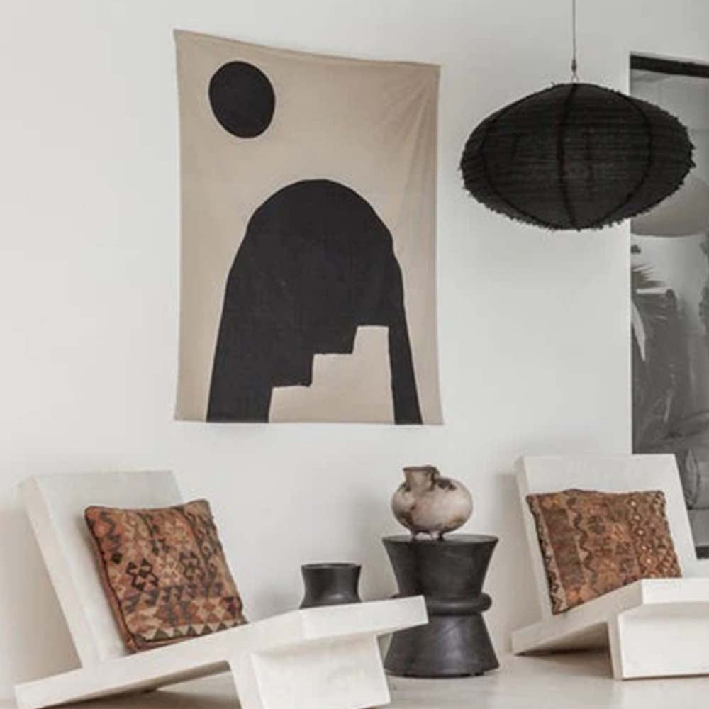 חלל מגורים מינימליסטי הכולל שני כיסאות לבנים, כריות מעוטרות, שולחן קטן, אגרטל קרמיקה, יצירת אמנות מופשטת על הקיר, ומנורת התליון המרשימה "אהיל תאורה פשתן שחור" מבית Fine Lab Home.