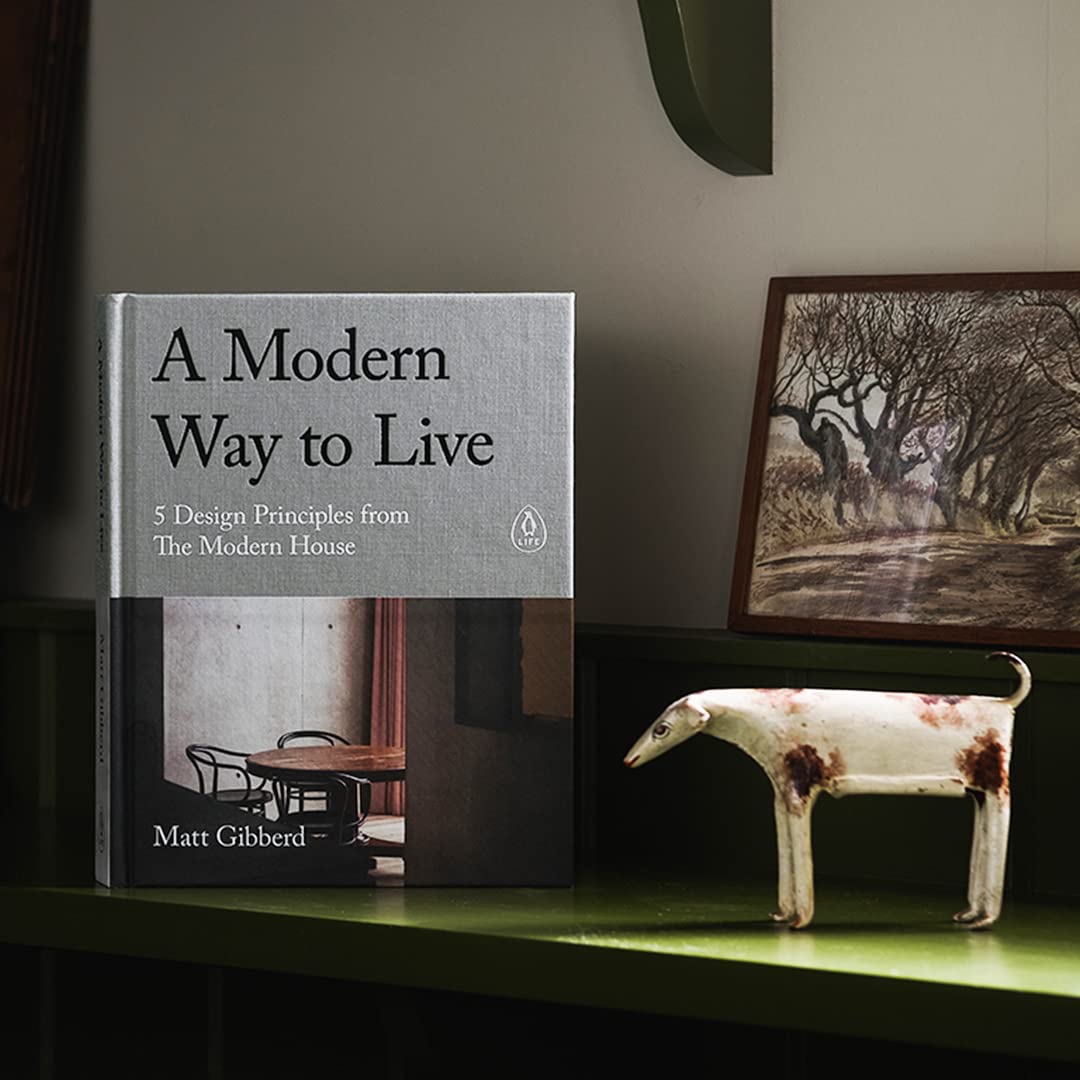 כריכת ספר העיצוב "modern way to live" מבית Fine Lab Home, עם שולחן עגול וכסאות בעיצוב מודרני מואר ברכות. כותרת המשנה: 5 עקרונות עיצוב של The Modern House לשיפור איכות החיים.