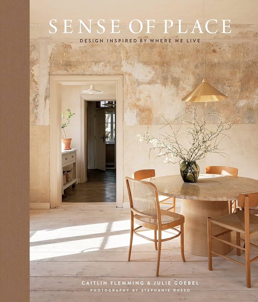 עטיפת הספר "ספר עיצוב sense of place" מאת Fine Lab Home, המציגה פינת אוכל כפרית עם ריהוט מעץ, קירות בהירים, אגרטל עם ענפים ואור טבעי רך. כולל את שם הספר ושמות המחברים.