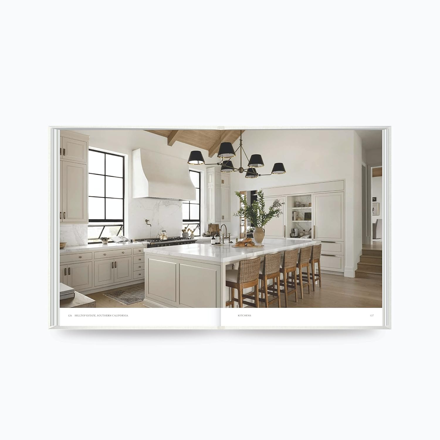 על עטיפת הספר "The Art of Home" מבית Fine Lab Home מופיעה אישה המסדרת פרחים במסדרון מואר בשמש, המשקפת את סגנון העיצוב האופייני למותג.