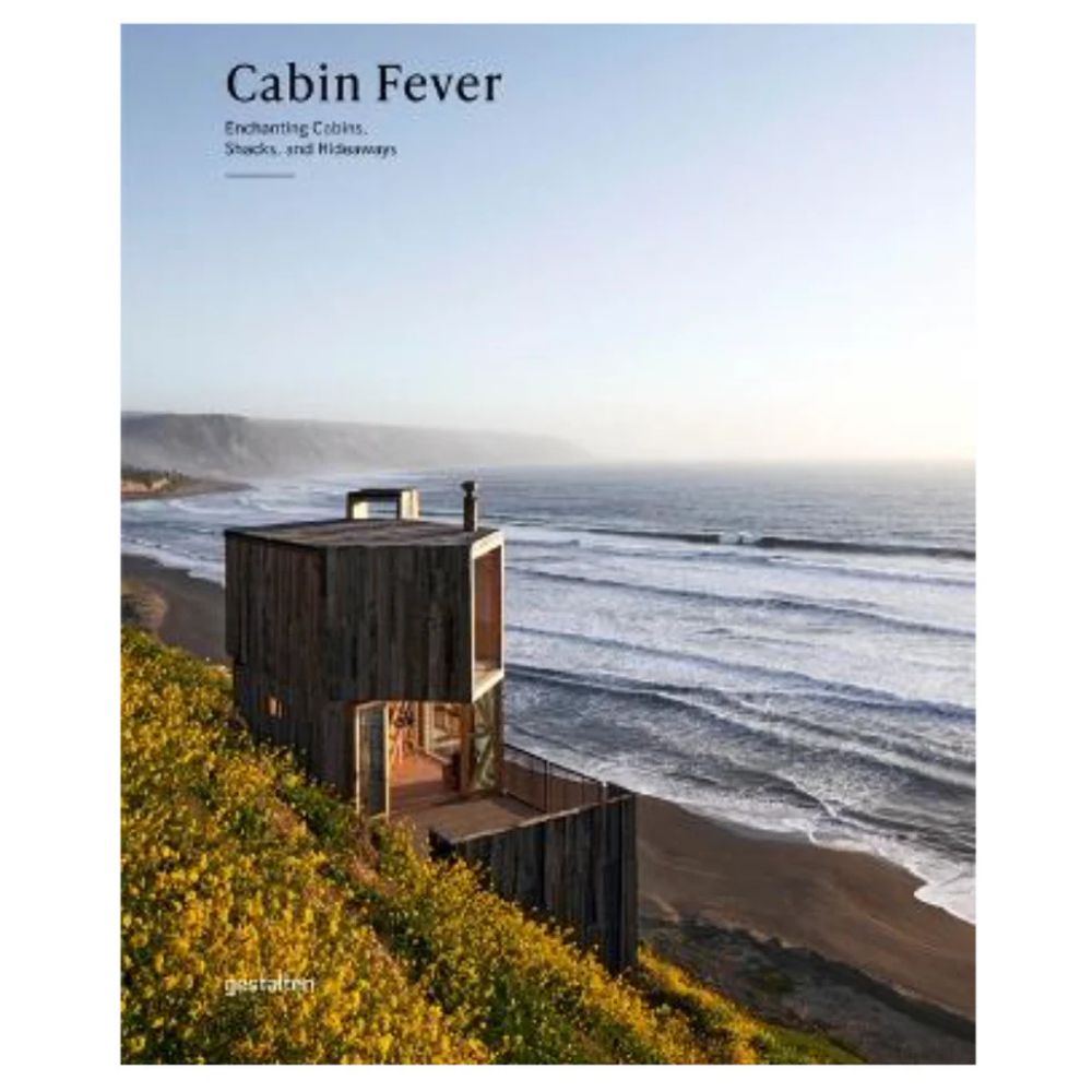 ספר העיצוב cabin fever מבית Fine Lab Home מציג בקתה מודרנית מעץ בעיצוב מינימליסטי על גבעה ירוקה המשקיפה אל הים, כפי שמופיעה על כריכת הספר.