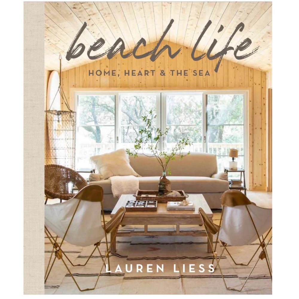 הכריכה של ספר העיצוב Beach Life מבית Fine Lab Home מציגה סלון עץ עם עיצוב פנים מדויק, ספות וכורסאות נוחות, שולחן קפה וחלונות גדולים שמכניסים אור טבעי לאווירת חיים חופיים.