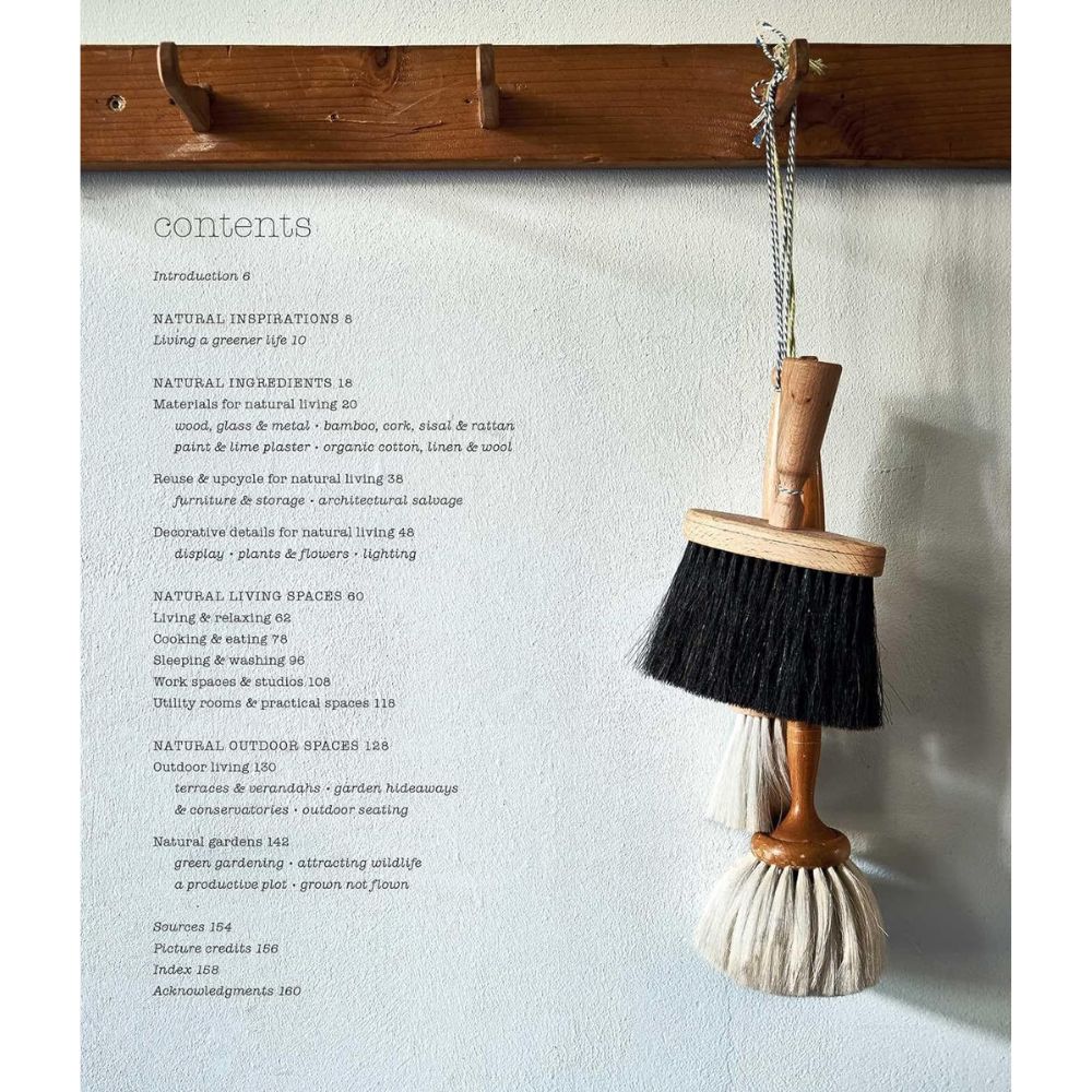 שתי מברשות עם זיפים טבעיים תלויות על קיר באמצעות שרשרת מתכת, ומוסיפות סגנון בר קיימא עם חומרים טבעיים לצד "ספר עיצוב naturally sustainable" של Fine Lab Home, הפתוח בעמוד התוכן המודפס עם כותרות הפרקים ומספרי העמודים.