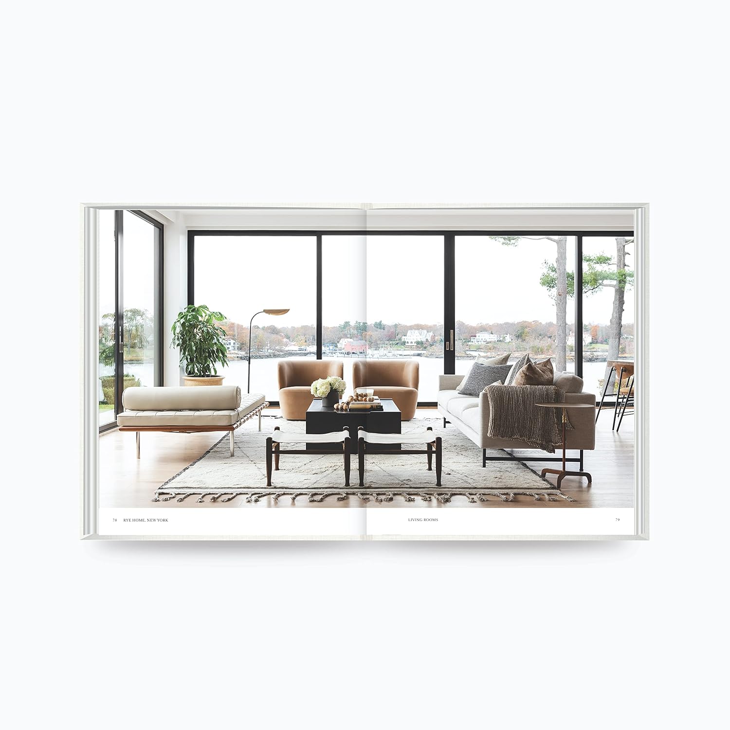 על עטיפת הספר "The Art of Home" מבית Fine Lab Home מופיעה אישה המסדרת פרחים במסדרון מואר בשמש, המשקפת את סגנון העיצוב האופייני למותג.