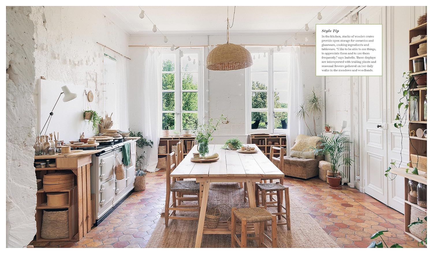 ענף עלים גדול באגרטל קרמי מונח על שרפרף עץ ליד מיטה מסודרת עם מצעים ניטרליים, המקשר בין הטבע לעיצוב הבית; מוצג: ספר עיצוב בית לכל עונות השנה מאת Fine Lab Home.