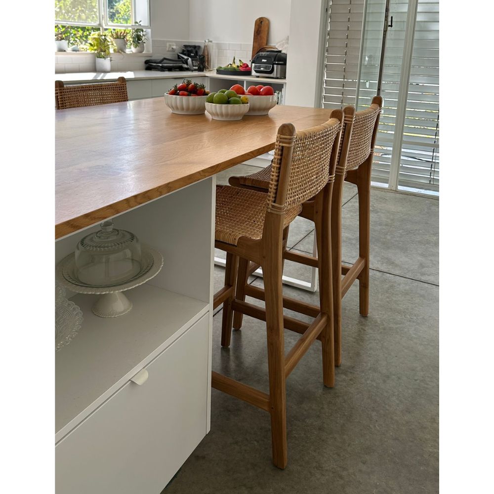 הכסא "כסא בר מעץ טיק וראטן טבעי" מבית Fine Lab Home, עם מושב ומשענת קלועים מראטן, מוצג על רקע לבן חלק.