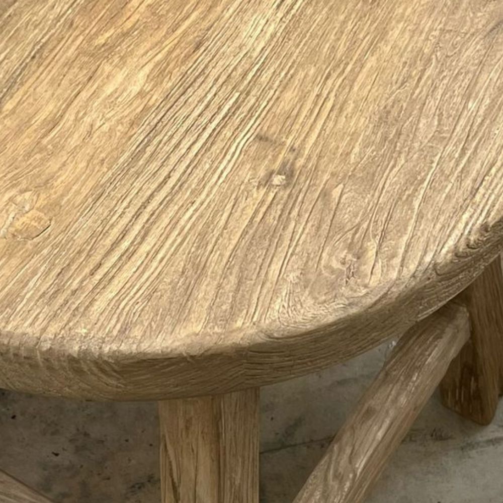 שולחן צד מעץ מלא עגול בעבודת יד, בעל מושב עגול וארבע רגליים אלכסוניות המחוברות בתמיכות רוחב, צולם על רקע לבן—מושלם כשולחן צד באווירה כפרית.