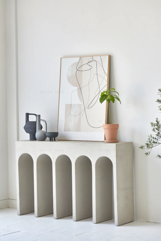 הקונסולה קשתות נורדית מבית Fine Lab Home כוללת חמש רגליים בצורת קשתות ומעוצבת עם ספרים מוערמים ושלושה אגרטלי קרמיקה ניטרליים, הניצבים על רקע קיר לבן חלק.