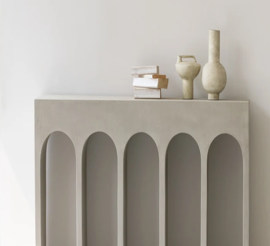 הקונסולה קשתות נורדית מבית Fine Lab Home כוללת חמש רגליים בצורת קשתות ומעוצבת עם ספרים מוערמים ושלושה אגרטלי קרמיקה ניטרליים, הניצבים על רקע קיר לבן חלק.