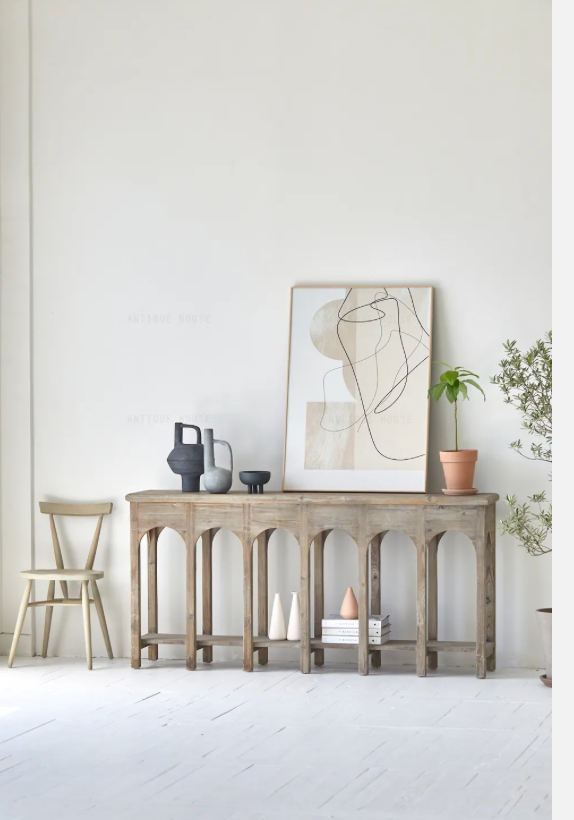 קונסולה נורדית עץ מבית Fine Lab Home ניצבת על רקע קיר לבן, מעוצבת עם שתי קערות, ספרים ערוכים ועיצוב דקורטיבי; לצדהן כיסא בר, תיק תלוי ועלה מיובש המוסיפים נגיעה מודרנית.