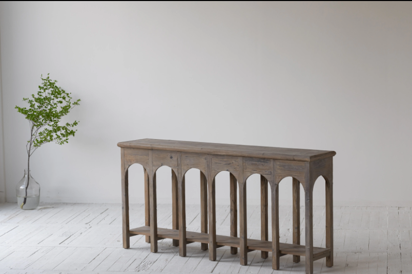 קונסולה נורדית עץ מבית Fine Lab Home ניצבת על רקע קיר לבן, מעוצבת עם שתי קערות, ספרים ערוכים ועיצוב דקורטיבי; לצדהן כיסא בר, תיק תלוי ועלה מיובש המוסיפים נגיעה מודרנית.