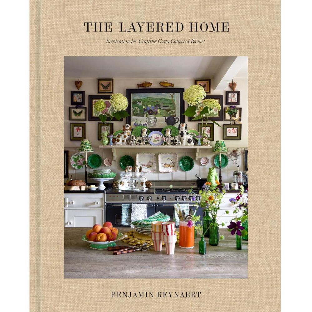 עטיפת הספר "The Layered Home" מאת Fine Lab Home, המציגה מטבח תוסס ואקלקטי המעוטר בצלחות נוי, פרחים טריים, סידורי פירות ויצירות אמנות ממוסגרות מעל הכיריים — סצנה מעוררת השראה המעניקה השראה לעיצוב הבית מתוך ספר עיצוב הבית המרהיב הזה.