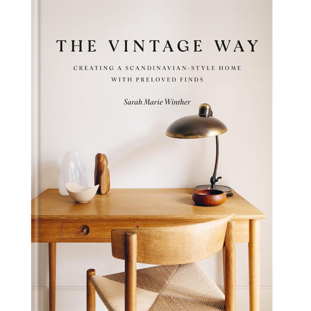 על כריכת ספר העיצוב "The Vintage Way" מבית Fine Lab Home נראים שולחן עץ, כיסא, מנורה וחפצי נוי בסגנון וינטג' על רקע קיר לבן — השראה לעיצוב פנים סקנדינבי לבית.