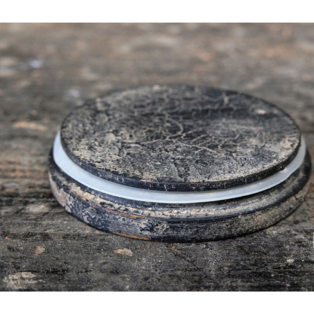 תחתית לכוס עגולה ושחורה עם מרקם מחוספס מונחת על משטח כהה לצד "צנצנת זכוכית עם מכסה עץ" של Fine Lab Home – שלושה גדלים.