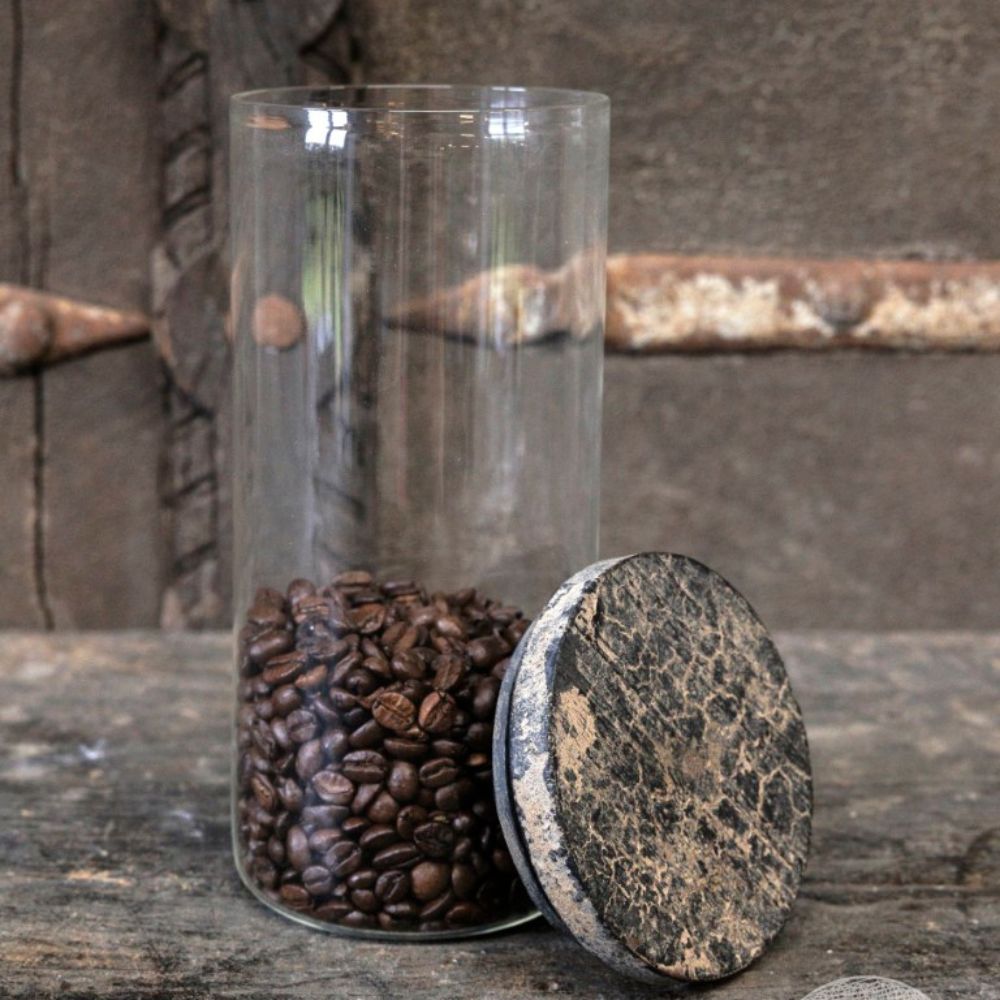 צנצנת זכוכית עם מכסה עץ מבית Fine Lab Home, חצי מלאה בפולי קפה, מוצגת על משטח כפרי כשהמכסה מונח לצידה.