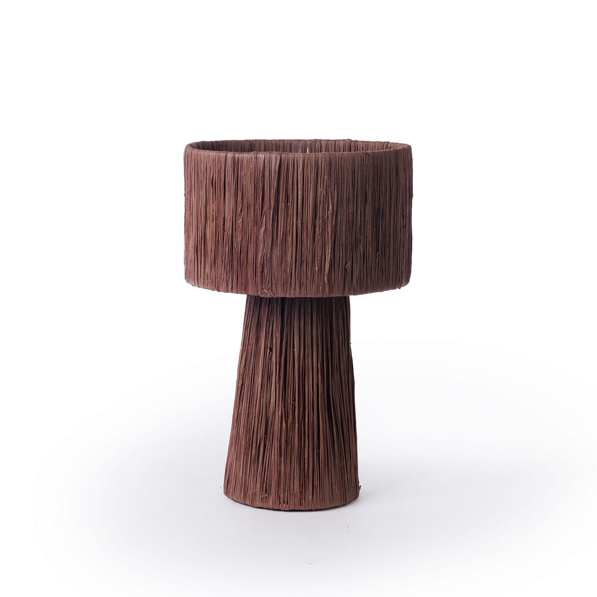 מנורת השולחן “רפיה” בצבע חום שוקולד של Fine Lab Home – 2 גדלים – כוללת מנורה חומה עם בסיס גלילי ואהיל בצורת תוף, שניהם עטופים בסיבים טבעיים בעלי מרקם אנכי. המנורה הדקורטיבית האלגנטית הזו, המוצגת על רקע לבן, מהווה תוספת מושלמת לכל חלל פנים מודרני.