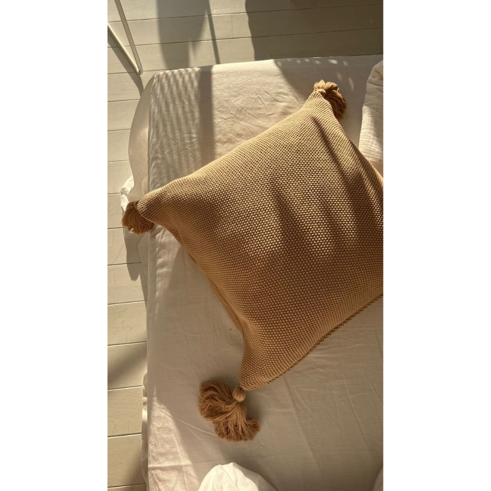 תקריב של מיטה עם מצעים לבנים וכרית נוי של Fine Lab Home בצבע חול עם ציצה בפינה.