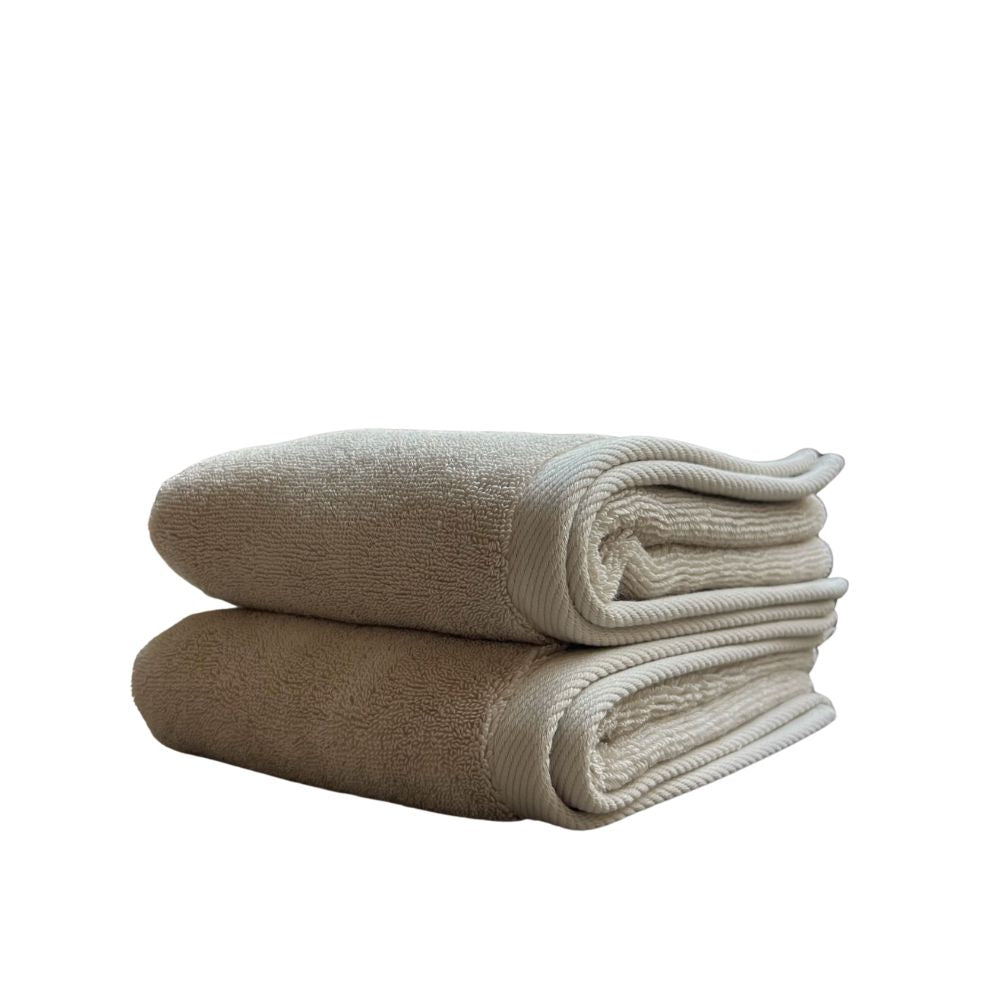 שתי מגבות זוג מגבות פנים/ידיים בצבע חול מבית Fine Lab Home מקופלות ומונחות זו על גבי זו על רקע לבן, ומדגישות את המרקם הרך והאיכות היוקרתית שלהן.