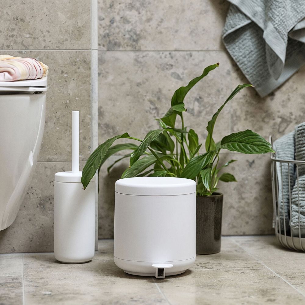 מברשת אסלה ume בשלושה צבעים מבית Fine Lab Home עם פח תואם על רצפת חדר האמבטיה, לצד צמח ירוק וסלסלה עם מגבות – שילוב מושלם לאביזרי אמבטיה בסגנון מודרני.