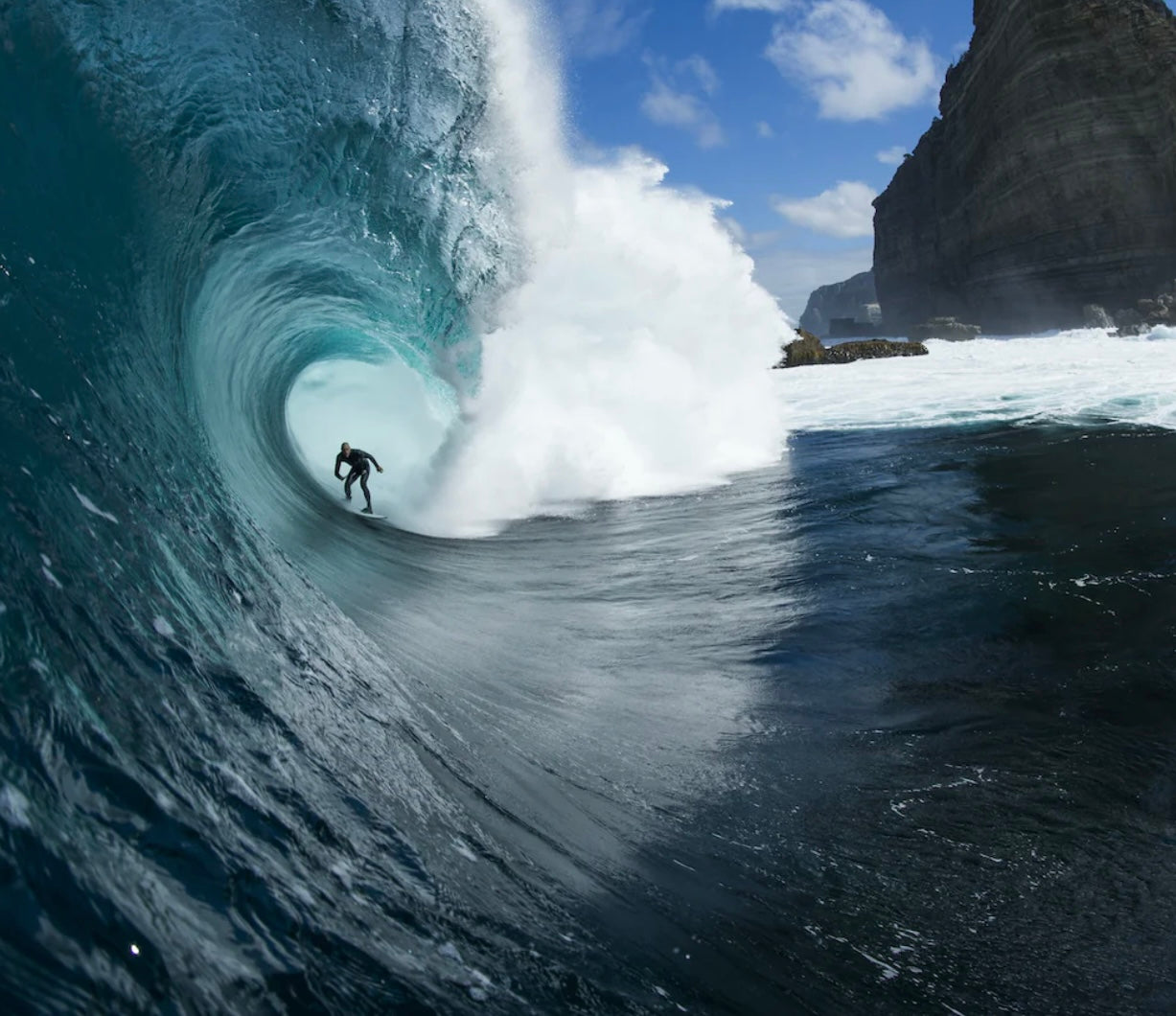 ספר העיצוב "The Surf Atlas" בכריכה קשה מבית Fine Lab Home כולל תמונת שער של גולש גלים בתוך גל כחול ענק.