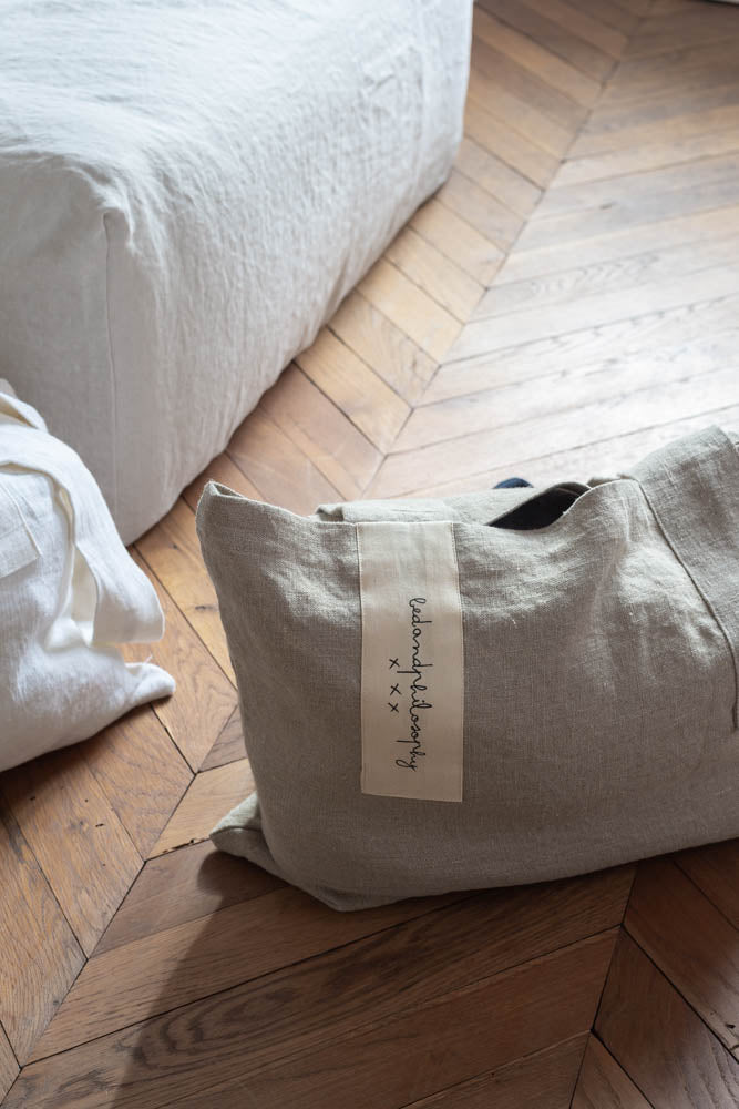 תיק פשתן של Fine Lab Home הוא תיק נשיאה מלבני בצבע לבן-שמנת, עם שתי ידיות רחבות ותווית קטנה בצבע בז' עם כיתוב בכתב יד.