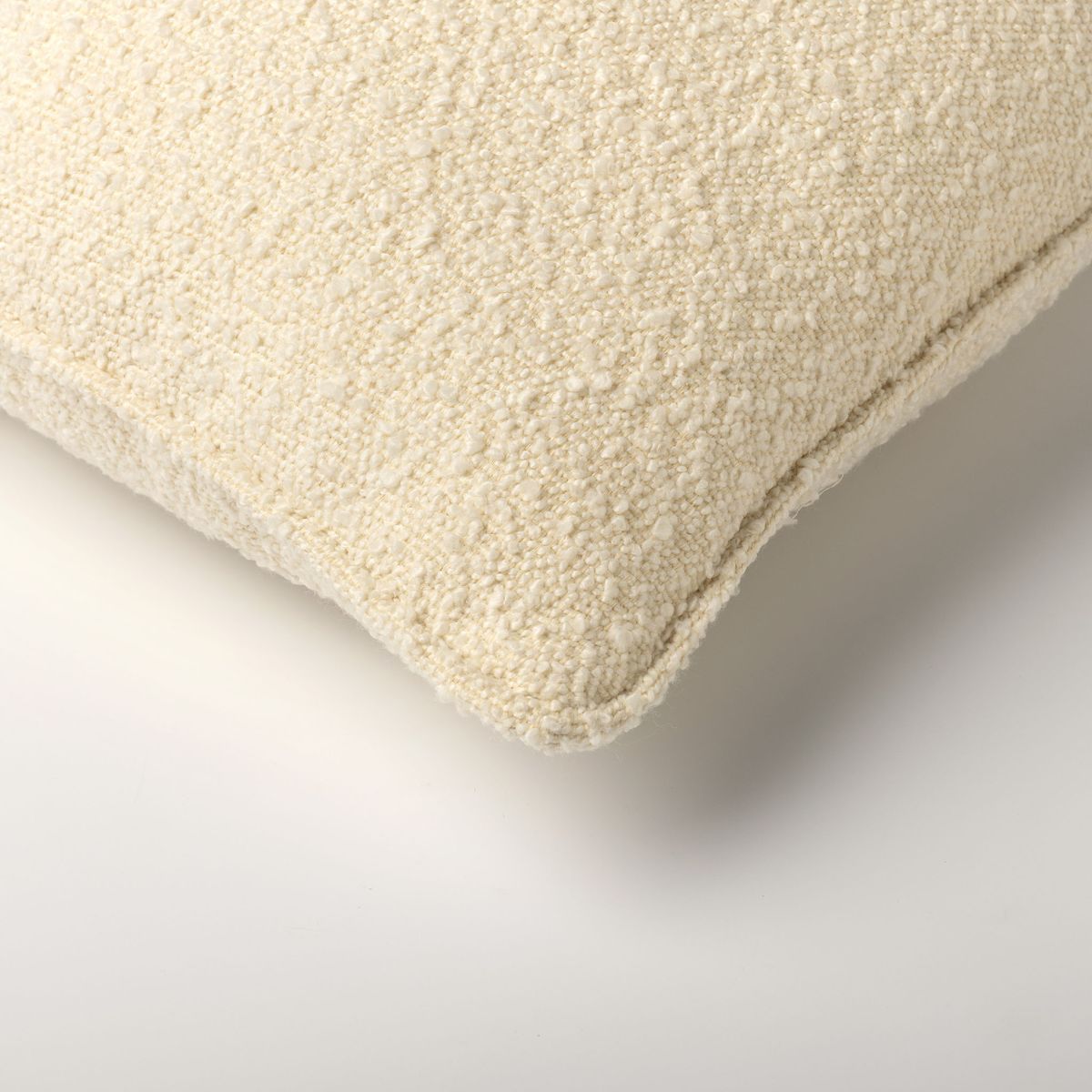 תקריב של פינת הכרית הדקורטיבית "Onno" מבית Fine Lab Home, המציגה את הבד המרקם בצבע לבן-שבור על רקע לבן.