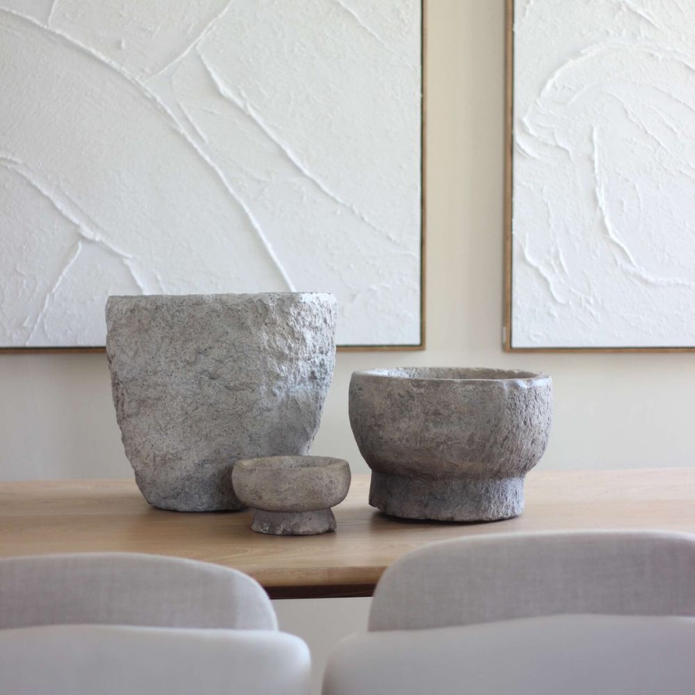 שלוש קערות כד דמוי אבן בטקסטורה טבעית מבית Fine Lab Home בגדלים שונים מסודרות על שולחן עץ, ומשלימות אותן יצירות אמנות מופשטות בלבן, לתוספת מודרנית לאוסף האקססוריז לבית שלכם.