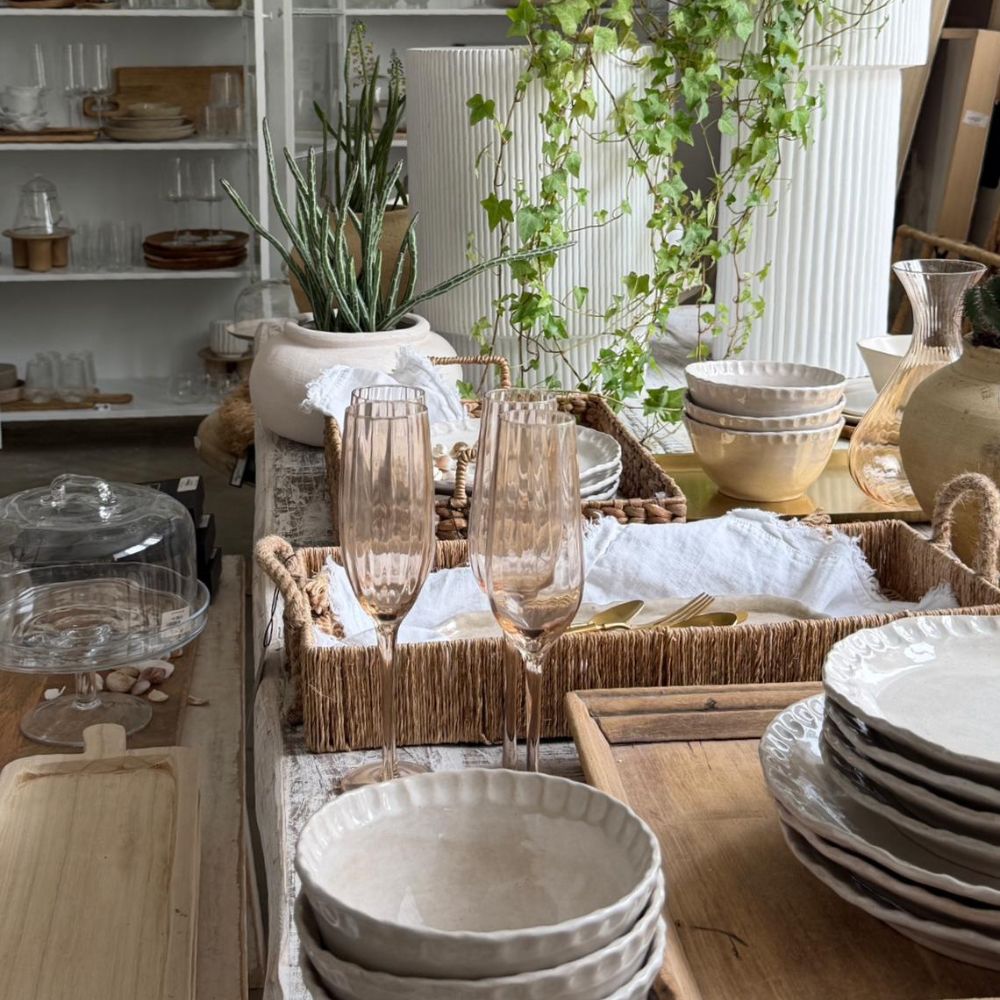 על שולחן כפרי ערוכים צלחות קרמיקה, מגשי עץ, סט של 6 כוסות שמפניה של Fine Lab Home בנפח 260 מ"ל, כלי זכוכית וסלים קלועים; עציצים ומדפים עמוסי כלים משלימים את התמונה האלגנטית.
