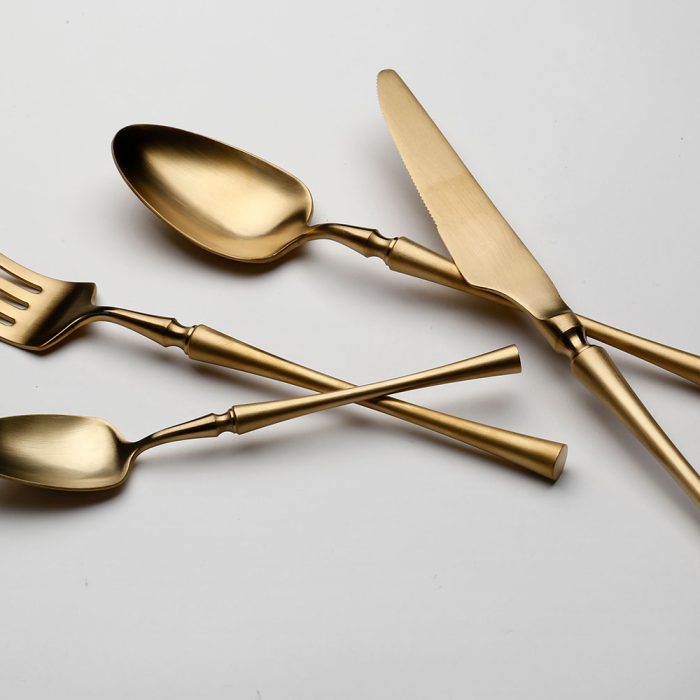 ארבעה כלי אוכל בצבע זהב — כף, מזלג, סכין וכפית — מסודרים על רקע לבן ומדגישים את סט סכו”ם 24 חלקים - זהב מבית Fine Lab Home, המושלם לחוויית אכילה אלגנטית.