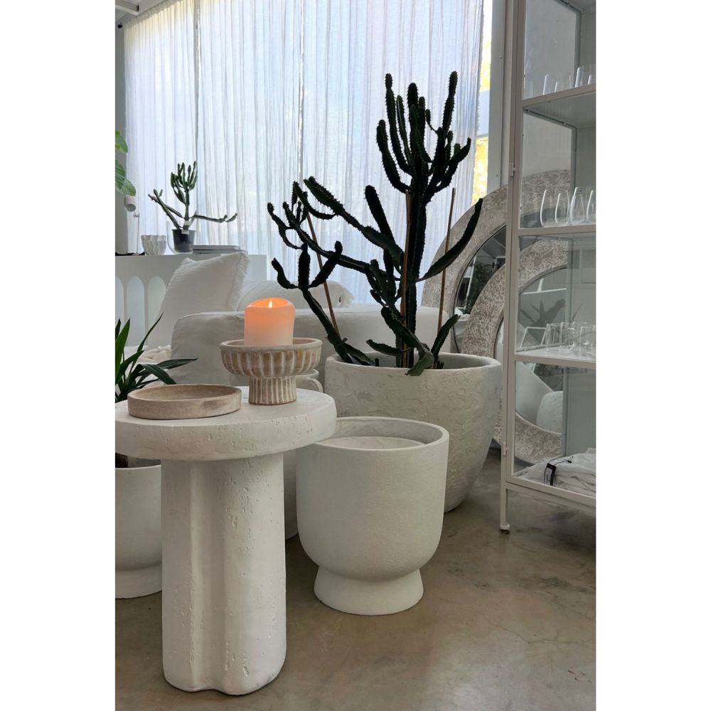 חדר מודרני ומינימליסטי עם עיצוב לבן, עציצי קקטוסים, נר דולק על Fine Lab Home סטול לבן- בסיס גליל, וכלי זכוכית המוצגים על מדף.