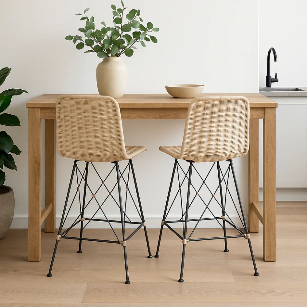 שני כיסאות בר ראטן אמיתי רגלי מתכת מבית Fine Lab Home מוצבים ליד שולחן עץ בהיר עם אגרטל ירוק וקערה, כשכיור מטבח ברקע, משדרגים כל אי מטבח לסטייל ופונקציונליות.