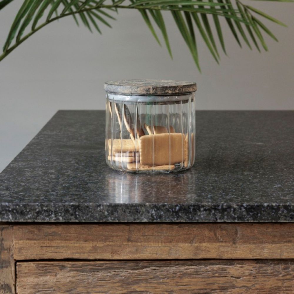 צנצנת זכוכית מפוספסת עם מכסה עץ בשני גדלים מבית Fine Lab Home מונחת על משטח אבן כהה, מלאה בעוגיות מלבניות, עם מגירת עץ בתחתיתה וצמח ירוק ברקע.