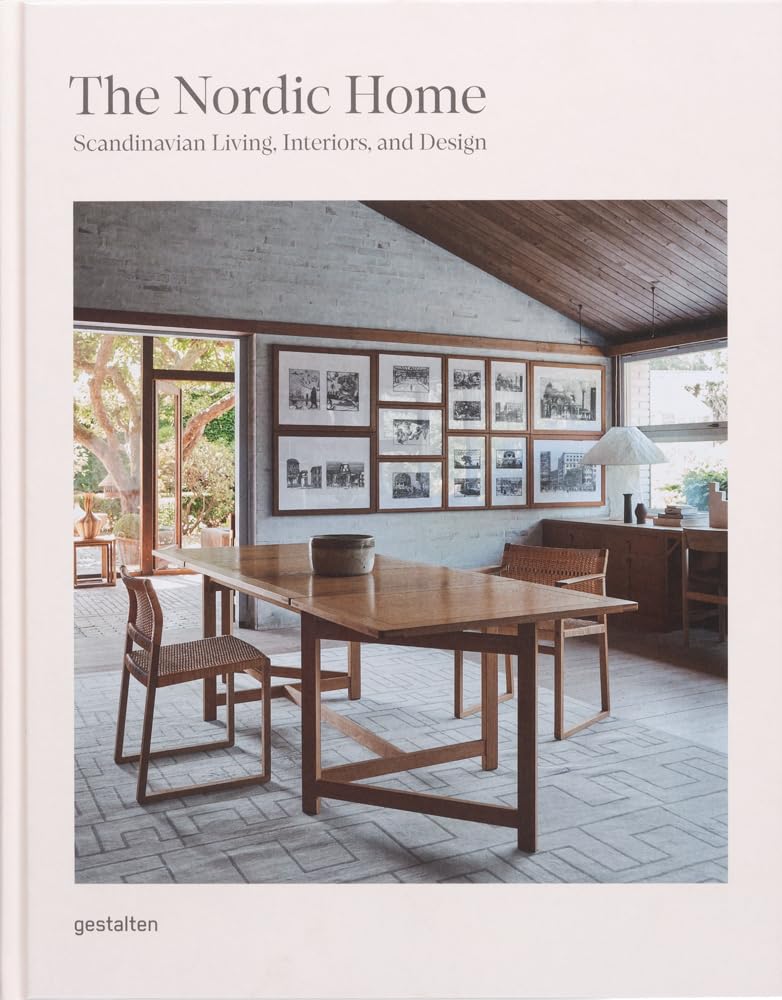ספר העיצוב The Nordic Home מבית Fine Lab Home מציג חדר אוכל סקנדינבי עם ריהוט עץ, יצירות קיר וחלונות גדולים, ומשקף עיצוב סקנדינבי ומינימליזם.