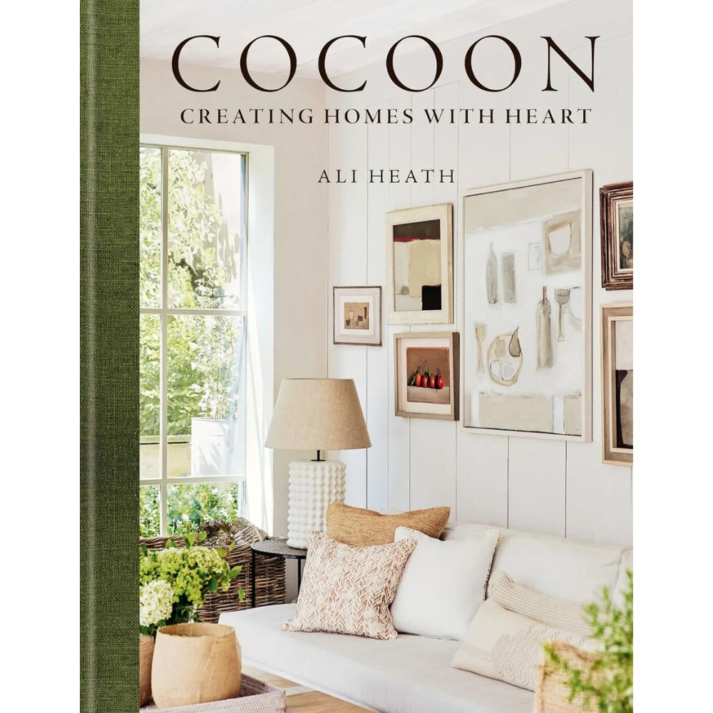 כריכת הספר ספר עיצוב cocoon מאת Fine Lab Home: סלון נעים עם ספה לבנה, כריות ניטרליות, תמונות ממוסגרות ומנורת שולחן ליד החלון — ספר השראה אמיתי לעיצוב.