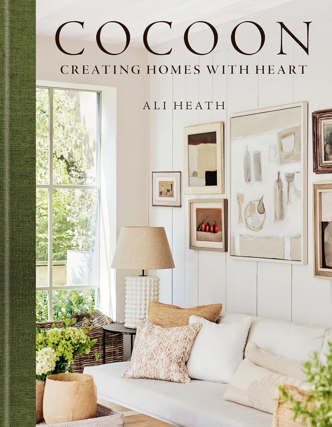 עטיפת הספר "עיצוב קוקון" של Fine Lab Home מציגה סלון נעים עם עיצוב ניטרלי, תמונות ממוסגרות וחלונות גדולים המדגישים את היופי הטבעי.